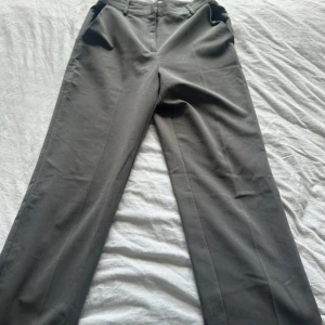 Grå kostymbyxor från NA-KD Reborn - Snygga grå kostymbyxor från NA-KD Reborn i klassisk rak modell. Byxorna har hög midja och vida ben, perfekta för en clean och stilren look. Tillverkade i ett mjukt material som känns bekvämt hela dagen.