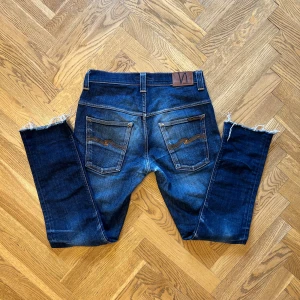 Nudie jeans - Snygga mörkblå jeans från Nudie med slitningar, jeansen är stilrena med riktigt fett tvätt! Storlek W32 L34 men passar mer som W31 L32. Modellen heter tape Ted. Säljer dessa för 799kr pga en utgående modell så den finns inte att köpa. Priser är ej hugget i sten!!!