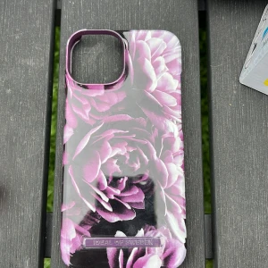 Blommigt mobilskal från iDeal of Sweden - Snyggt mobilskal med lila och vita blommor från iDeal of Sweden. Skalet har en glansig finish och är designat för att passa en mobil med stor kameraöppning. Insidan är beige och mjuk för extra skydd. Perfekt för dig som vill ha en unik look på mobilen.