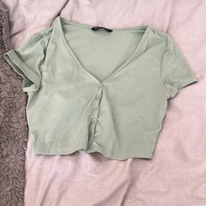 Ljusgrön bolero från SHEIN - Säljer en ljusgrön bolero från SHEIN med korta ärmar och v-ringning. Toppen har knappar framtill och är gjord i mjuk bomull. Perfekt för dig som gillar en enkel men trendig stil.