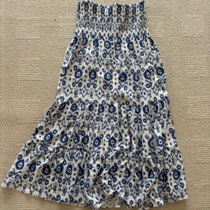 Blåvit mönstrad klänning från Zara - Supersöt blåvit kjol/ klänning från Zara med smock upptill och volang i nederdelen. Klänningen har ett unikt mönster i blått på vit botten och är axelbandslös. 