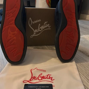 Christian Louboutin mörkblå sneakers - Snygga mörkblå sneakers från Christian Louboutin med klassisk röd sula och diskret logga. Skorna har snörning och är tillverkade i mocka med svarta detaljer. Perfekta för dig som vill ha en lyxig och stilren look med en ikonisk touch. Tyvärr tillkommer inte allt som syns på bilderna
