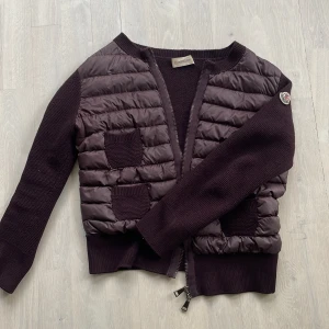 Vinröd Moncler cardigan med dragkedja - Rensar min garderob så säljer en vinröd unik cardigan från Moncler med puffig framsida och två stickade fickor.❤️Koftan har långärmade stickade ärmar, ribbade muddar och dragkedja framtill. Perfekt för lager-på-lager under höst och vinter. Storleken är XL men har krymt i tvätten så passar mig som bär S. Jag är ca 165 cm lång! Den är i mycket bra skick, men säljer för ungefär halva priset av inköpspriset.