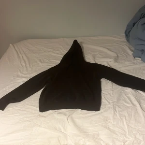 Svart hoodie med tryck och huva från bastille - Svart hoodie med stor färgstark print på ryggen som visar en brinnande bil och texten 'MIAMI DOOMY BEACH'. Klassisk modell med huva och långa ärmar. Mjuk insida och ribbade muddar. Perfekt för dig som gillar streetwear och unika motiv.