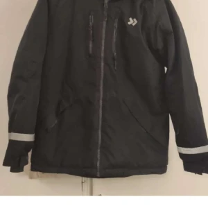 Svart vindjacka från 157 Funk, strl 160 - Svart vindjacka från 157 Funk med reflekterande detaljer på ärmar och rygg. Jackan har dragkedja framtill, flera fickor med dragkedja och en sportig look. Perfekt för blåsiga dagar och utomhusaktiviteter.
