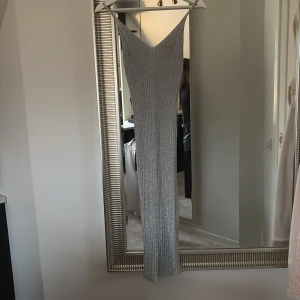 Silvrig långklänning från H&M XS - Supersnygg långklänning från H&M i storlek XS. Klänningen är silvrig med glittrigt ribbat mönster och har en v-ringad hals samt smala axelband. Materialet är syntet och ger en cool metallic-look som verkligen sticker ut. Perfekt för dig som vill glänsa lite extra!