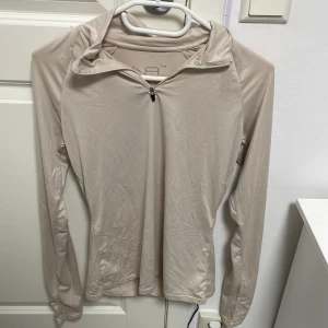 beige träningstt  - Sportig beige långärmad träningströja från NA med half zip och huva. Tillverkad i mjukt och stretchigt syntetmaterial som andas, perfekt för löpning eller gym. Slimmad passform och stilren look, passar dig som gillar minimalistisk stil. och ett barn strechiga träningsshort i samma förg och matrial