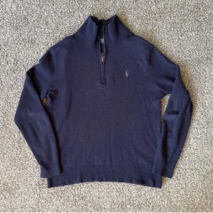 Mörkblå half zip tröja Polo Ralph Lauren - Mörkblå långärmad tröja i merinoull från Polo Ralph Lauren med half zip och broderad logga på bröstet. Det förekommer 1 litet hål på båda ärmarna ungefär vid armbågen. (Se bilder) Förutom det är den i bra skick!