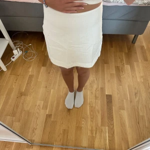 Vit linnekjol med dragkedja - Snygg vit kortkjol i linne med enkel och stilren design. Kjolen har en diskret dragkedja bak och är lätt utsvängd för en avslappnad look. Perfekt till varma dagar och enkel att matcha med crop tops eller t-shirts.