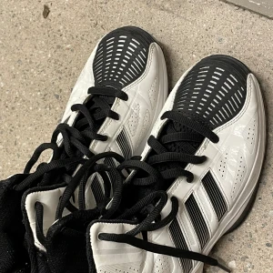 Svarta och vita Adidas sneakers strl 40 - Snygga Adidas sneakers i svart och vitt med coola grafiska detaljer och klassiska ränder på sidorna. Skorna har snörning, rund tå och en slitstark syntetsula. Perfekta för dig som gillar sportig stil och vill sticka ut med ett unikt mönster.