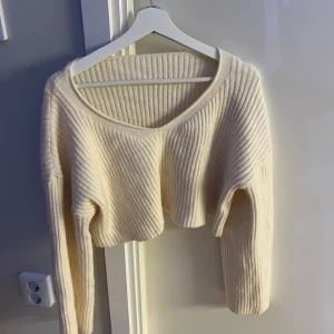 Ljusbeige croppad stickad tröja - Superfin croppad stickad tröja i ljusbeige med breda ribbade ränder. Tröjan har v-ringning och långa ärmar med lite vidare passform. Perfekt att styla med höga jeans eller kjol för en chill look.