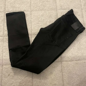 Svarta Replay Anbass jeans, stl 31 - Säljer ett par svarta Replay Anbass jeans i storlek 31. De har en slim passform med klassisk femficksdesign och snyggt svart läderpatch bak. Jeansen är tillverkade i stretchigt bomullsmaterial för extra  och sitter riktigt snyggt på.små i storlekarna