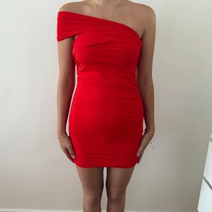 Röd one shoulder kortklänning - Snygg röd kortklänning med one shoulder-design och draperad effekt. Klänningen är tight och figurnära, perfekt för dig som vill sticka ut. Materialet känns stretchigt och följsamt. Enkel men ändå riktigt trendig look.