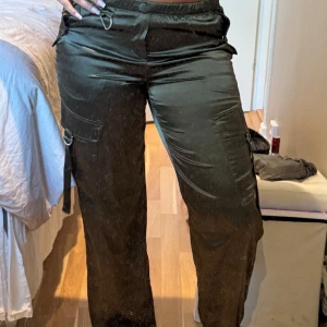 Gröna satin cargo pants S - Snygga gröna cargobyxor i glansigt satinmaterial från H&M. Byxorna har resår i midjan, flera fickor och coola metalldetaljer. Perfekt för dig som vill ha en trendig och bekväm look med streetkänsla. Aldrig anvönda
