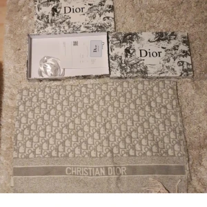 Beige halsduk från Christian Dior - Lyxig beige halsduk från Christian Dior med ikoniskt monogrammönster och tydlig logga längs kanten. Halsduken har fransar i ändarna och känns både klassisk och trendig. Perfekt accessoar för att lyfta din outfit.