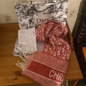 Röd halsduk från Christian Dior - Snygg röd halsduk från Christian Dior med vit logga och mönster. Halsduken har fransar i ändarna och ett klassiskt Dior-mönster i vitt och rött. Perfekt accessoar för att lyfta din outfit med lyxig vibe.