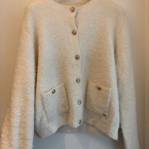 Vit fluffig kofta med fickor - Supermjuk och fluffig vit kofta med snygga guldknappar framtill och två praktiska fickor. Koftan är köpt för 2 år sedan på Kappahl för 500kr men knappt kommit till användning. Koftan har rund halsringning och lång ärm, perfekt för lager-på-lager och chill dagar. Passformen är normal och materialet känns riktigt cozy. Men måste dock tillägga att den har några skavanker, men skulle gissa på att dem gör bort! Ingenting man tänker på☺️ 