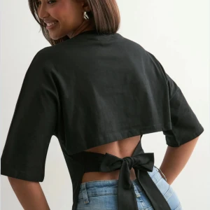 tilda törnqvist gamla Nelly knyt topp/ tshirt - Köpte den på sellpy. Svart croppad topp med korta ärmar och öppen rygg som knyts med en stor rosett baktill. T-shirttyp i mjukt material, perfekt för en trendig look. Snygg att matcha med jeans eller kjol.