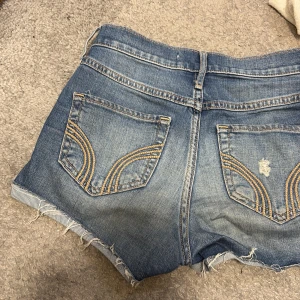 Hollister jeansshorts med slitna detaljer💕 - Snygga blå jeansshorts från Hollister med slitna detaljer och fransig kant. Klassisk femficksmodell med coola sömmar på bakfickorna. Perfekta för sommaren och ger en avslappnad vibe. Storlek W24💕