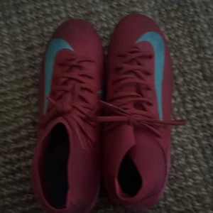 Nike Mercurial röda fotbollsskor acedemy - Säljer ett par Nike Mercurial fotbollsskor i röd färg med turkosa detaljer och snörning. Skorna har en spetsig tå och platt sula med turkosa dobbar för grymt grepp på planen. Tillverkade i syntetmaterial och har en sportig, slimmad design som sticker ut.  Skorna är använda 7-10 gånger innan dem blev för små. Mvh Ville 