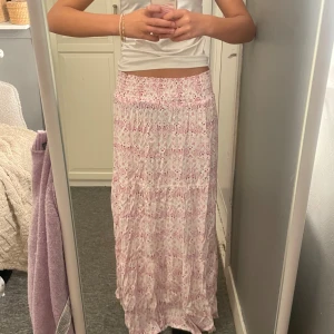 Långkjol med rosa mönster från lager 157 XS🩷 - Supersöt långkjol från 157 i vitt med rosa mönster storlek XS. Kjolen har smock i midjan för en bekväm passform och är gjord i ett lätt och luftigt bomullstyg. Perfekt för varma dagar när du vill ha en chill och romantisk look.