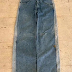 Wide jeans från Anvil med gator-detalj - Blåa wide jeans från Anvil med cool gator-patch på bakfickan och breda ben. Klassisk femficksmodell i 100% bomull med ljusare sidor och vintage-vibe. Perfekta för dig som gillar loose fit och streetstyle.