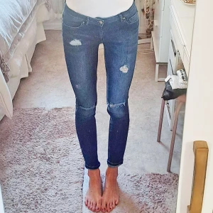 Mörkblå skinny jeans med slitningar - Säljer ett par mörkblå skinny jeans från hm. Jeansen har slitningar på låren och knäna. Jeansen har klassisk femficksdesign och sitter tight hela vägen ner. Perfekta för dig som gillar en smal siluett och lite ruffig look. Märket på baksidan är en slitning på fickan som ska vara där (syns dåligt på bild. Jag är 1,72. Storlek 36 så lite stora för mig i midjan. 