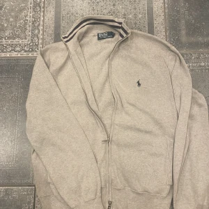 Beige ziptröja från Polo Ralph Lauren - Grå ziptröja från Polo Ralph Lauren, lappen har lossnat på halft på insidan men annars i bra skick