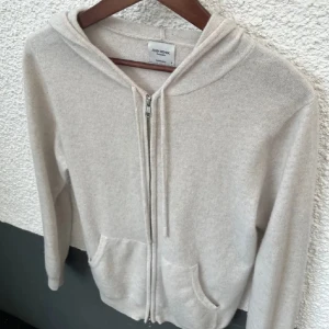 Vit  kashmirhoodie från John Henric - Mjuk och lyxig vit  hoodie i kashmir från John Henric. Tröjan har dragkedja, huva med snören och två fickor framtill. Perfekt för dig som gillar en clean och stilren look med premiumkänsla.