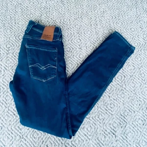 Replay mörkblå jeans straight fit - Snygga mörkblå jeans från Replay med klassisk femficksdesign och raka ben. Jeansen har kontrastsömmar och en läderpatch med Replay-logga bak i midjan. Materialet är slitstarkt jeans och passformen är normal med straight fit. Perfekt för dig som gillar stilrena och tidlösa jeans.