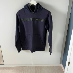 Mörkblå hoodie från Sail Racing - Säljer en mörkblå hoodie från Sail Racing med logga på bröstet och broderad text på luvan den är i helt okej skick hör av vid minsta lilla!