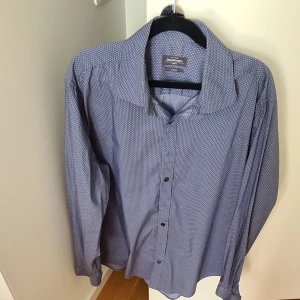 Slim fit mönstrad skjorta Dressmann - Snygg slim fit skjorta från Dressmann i blått med smått geometriskt mönster. Skjortan har klassisk krage, långa ärmar och knäppning framtill. Stretchigt material som ger en bekväm passform. Perfekt för dig som gillar stilrena detaljer.