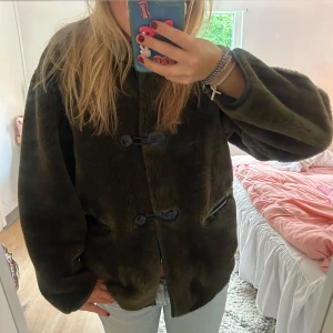 Mörkgrön pälsjacka med knappar - Säljer en mysig mörkgrön pälsjacka med oversized passform och stora knappar framtill. Jackan har två fickor och är tillverkad i ett mjukt, pälsliknande material. Perfekt för kalla dagar och ger en cool vibe till din outfit.