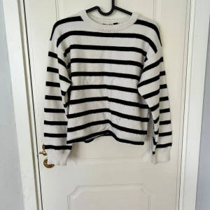 Randig stickad tröja XOXO friends - Säljer en mysig stickad tröja från XOXO friends i vitt med svarta horisontella ränder. Tröjan har rund halsringning, långa ärmar och ribbade muddar. Perfekt för dig som gillar klassisk stil med en twist.