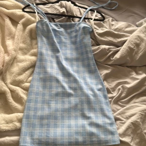 Blåvit rutig klänning från SHEIN - Supersöt blå och vit rutig kortklänning från SHEIN med smala axelband som knyts på axlarna. Klänningen har en figurnära passform och är perfekt för varma dagar. Materialet känns lätt och bekvämt mot huden.