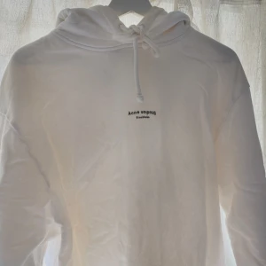 Vit hoodie från Acne Studios - Säljer en stilren vit hoodie från Acne Studios med liten logga på bröstet. Tröjan har huva med dragsko och långa ärmar. Perfekt för en avslappnad och trendig look.