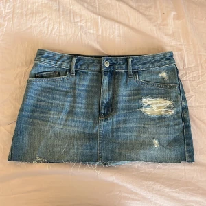  jeanskjol - Säljer en blå jeanskjol från Hollister med slitna detaljer framtill. Kjolen är lågmidjad. 
