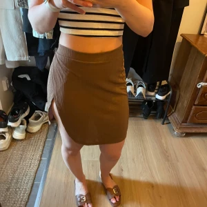 Brun omlottkjol från Bianca x Nelly - Säljer en brun kort omlottkjol från Bianca x Nelly i ribbat material. Kjolen har en slits på sidan och en figurnära passform som ger en snygg siluett. Perfekt att styla med crop tops eller t-shirts.