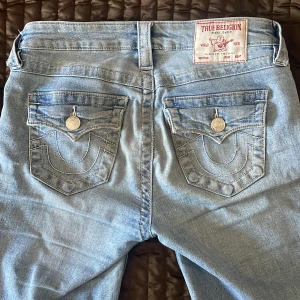 Ljusblå jeans från True Religion bootcut  - Säljer ett par ljusblå jeans från True Religion med klassiska bakfickor och silverfärgade knappar. Jeansen har normal passform och är tillverkade i denim.  Jätte snygga passar med allt får massa komplimanger 