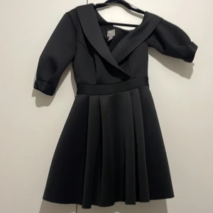 Svart klänning med krage från ASOS - Säljer en svart klänning från ASOS med bred krage och trekvartsärm. Klänningen har markerad midja och vidd i kjolen, vilket ger en klassisk siluett. Perfekt för dig som gillar stilrena och eleganta plagg. Jätte bra material med jätte bra skick! 