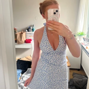Blommig halterneckklänning från H&M Divided - Supersöt vit halterneckklänning med blått blommönster från H&M Divided. Klänningen har knyt i nacken, djup v-ringning och är ärmlös. Perfekt för varma dagar och somriga tillfällen. Hör av er vid frågor eller fler bilder!💛