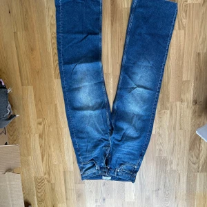 Blå jeansbyxor från Mango - Säljer ett par långa, raka, vida, blå jeansbyxor från MNG (Mango) och knappgylf. Jeansen har en normal/lösare passform och är tillverkade i denim. Perfekta för dig som gillar en tidlös stil. Långa i benen därav lite slitna i nedkant baktill 