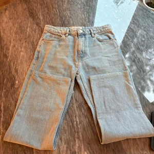 Ljusblå raka jeans - Säljer ett par ljusblå jeans med raka ben och klassisk femficksdesign. Jeansen har bälteshällor och en brun patch bak i midjan. Perfekta för en avslappnad stil och passar till det mesta.