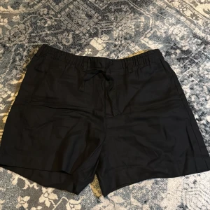 Svarta linneshorts från Zara - Snygga svarta shorts från Zara i 100% linne. De har en normal passform med elastisk midja och snörning för extra komfort. Perfekta för varma dagar när du vill ha en stilren och luftig look.