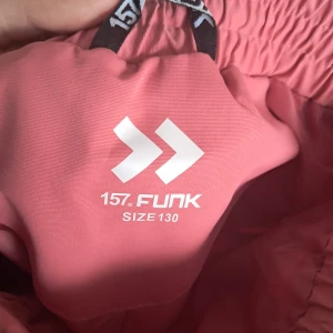 Rosa täckbyxor från 157 Funk - Säljer ett par rosa täckbyxor från 157 Funk i storlek 130. Byxorna har resår i midjan, justerbara hängslen och en ficka med lock på ena benet. Perfekta för kalla dagar utomhus.