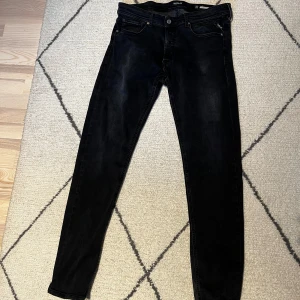 Svarta jeansbyxor från Replay - Säljer ett par svarta Replay jeansbyxor med klassisk femficksdesign och raka ben. Byxorna har knappgylf och diskreta sömmar på bakfickorna. Midjemått W34 och längd L34. Perfekta för dig som gillar stilrena och tidlösa jeans.