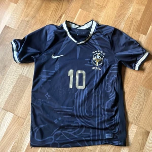 Brasilien fotbollströja Neymar Jr 10 - Säljer en svart Brasilien fotbollströja från Nike med Neymar Jr och nummer 10 i guld. Tröjan har korta ärmar, guldiga detaljer och Brasilien-emblem på bröstet. Tillverkad i Dri-FIT material för bra komfort. tar emot byten och kan diskutera pris vid snabb affär.