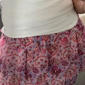 Rosa volangkjol med mönster - Supersöt kortkjol i rosa och lila toner med volanger . Kjolen har flera lager. Resår i midjan för skön passform