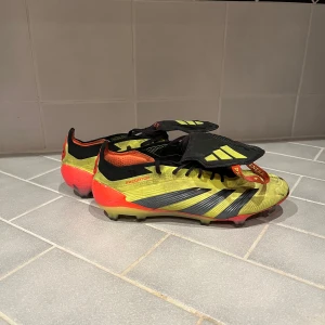 Adidas Predator fotbollsskor i gul och röd - Säljer ett par Adidas Predator fotbollsskor i en cool gul och röd färg med svarta detaljer. Skorna har snörning och en låg profil, perfekt för dig som vill ha bra grepp och kontroll på planen. Snygg design med klassiska Predator-detaljer. Skada på skon, se bilder.