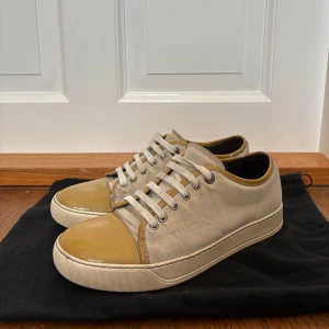 Lanvin  - Snygga beige sneakers från Lanvin med ovandel i mocka och detaljer i ljusbrunt skinn. Skorna har vita snören, rund tå och platt sula. Perfekta för dig som gillar stilrena och klassiska sneakers med en twist. Pris kan diskuteras!